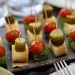 Colorful appetizers featuring cherry tomatoes, pickles, and rolled wraps on skewers.